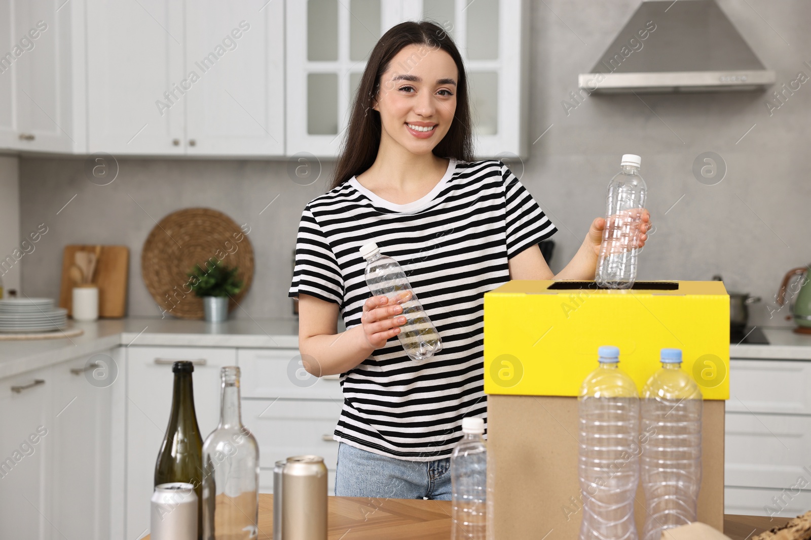 Photo of Smiling woman separating garbage at table in kitchen