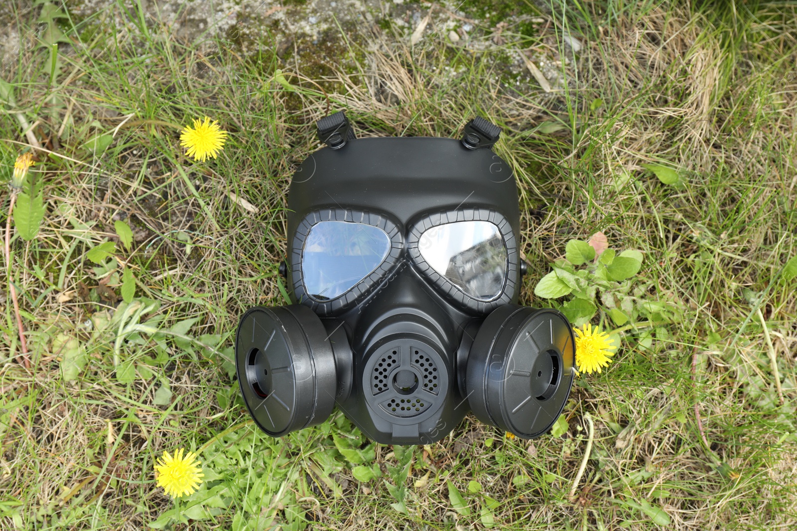 Photo of One gas mask on green grass outdoors, top view