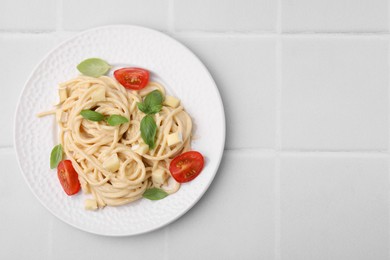 Photo of Delicious pasta with brie cheese, tomatoes and basil leaves on white tiled table, top view. Space for text
