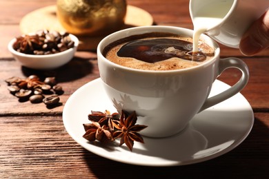 Woman pouring milk into cup of coffee with anise stars at wooden table