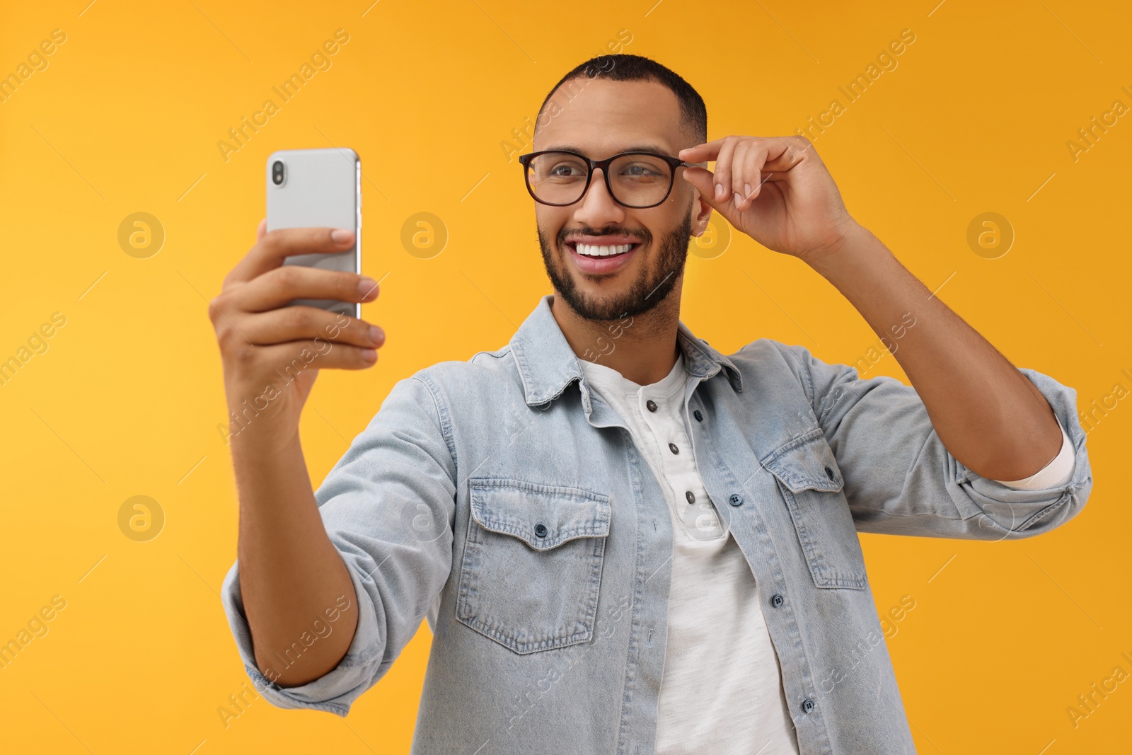 Photo of Smiling young man taking selfie with smartphone on yellow background