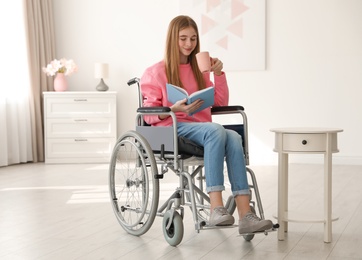 Teenage girl with book and drink in wheelchair at home