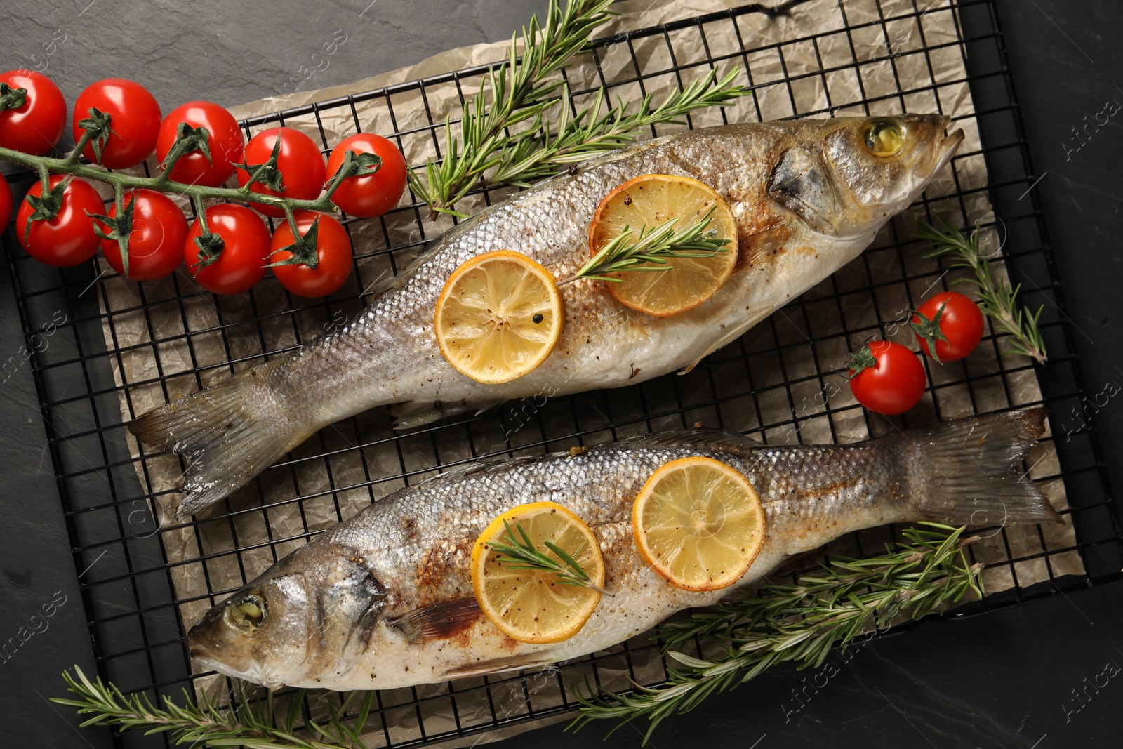 Photo of Baked fish with tomatoes, rosemary and lemon on black textured table, top view