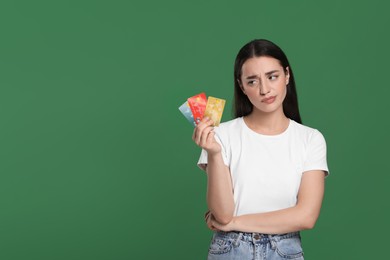 Confused woman with credit cards on green background, space for text. Debt problem