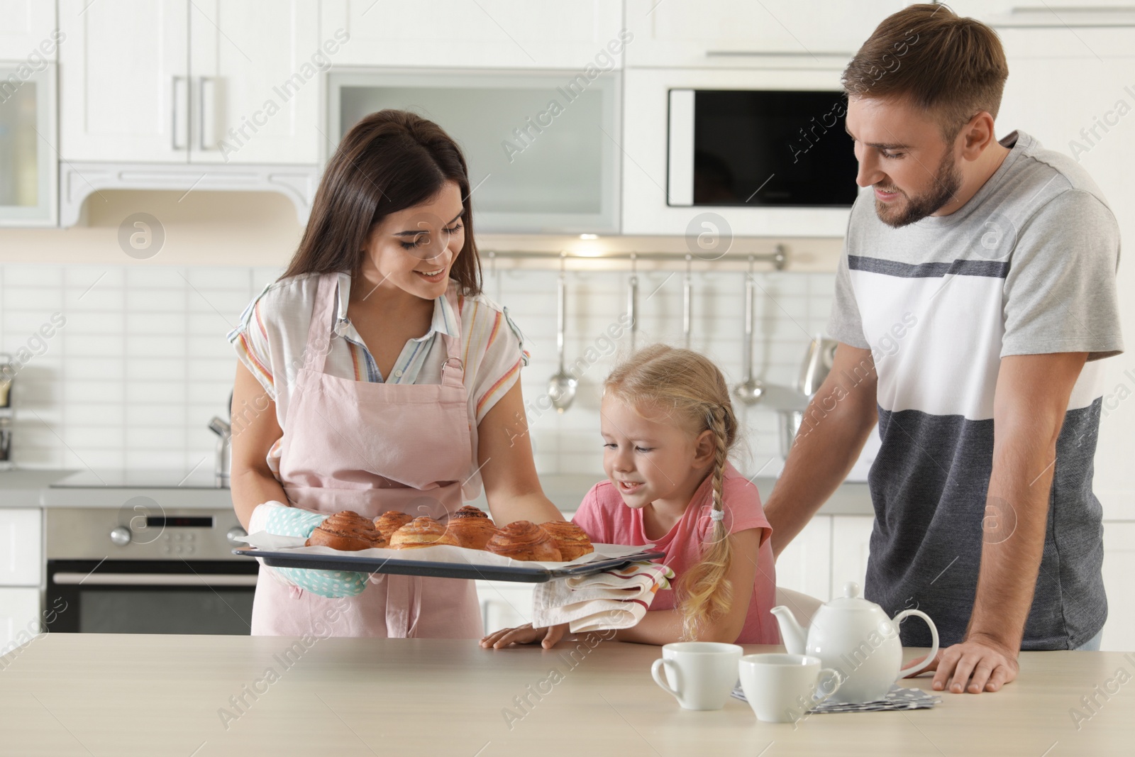 Photo of Young beautiful woman treating her family with freshly oven baked buns in kitchen