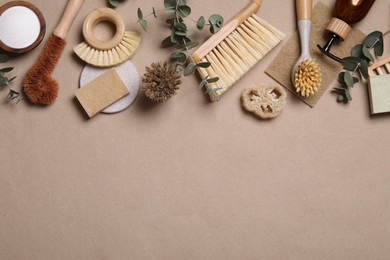 Photo of Cleaning brushes, baking soda, soap, sponges and eucalyptus on pale brown background, flat lay. Space for text