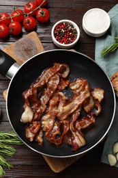 Delicious bacon slices in frying pan and products on wooden table, flat lay