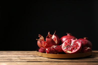 Photo of Tray with ripe pomegranates on table against black background, space for text