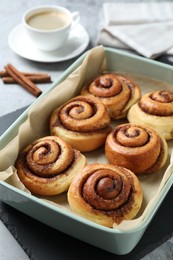 Photo of Baking dish with tasty cinnamon rolls on grey table, closeup