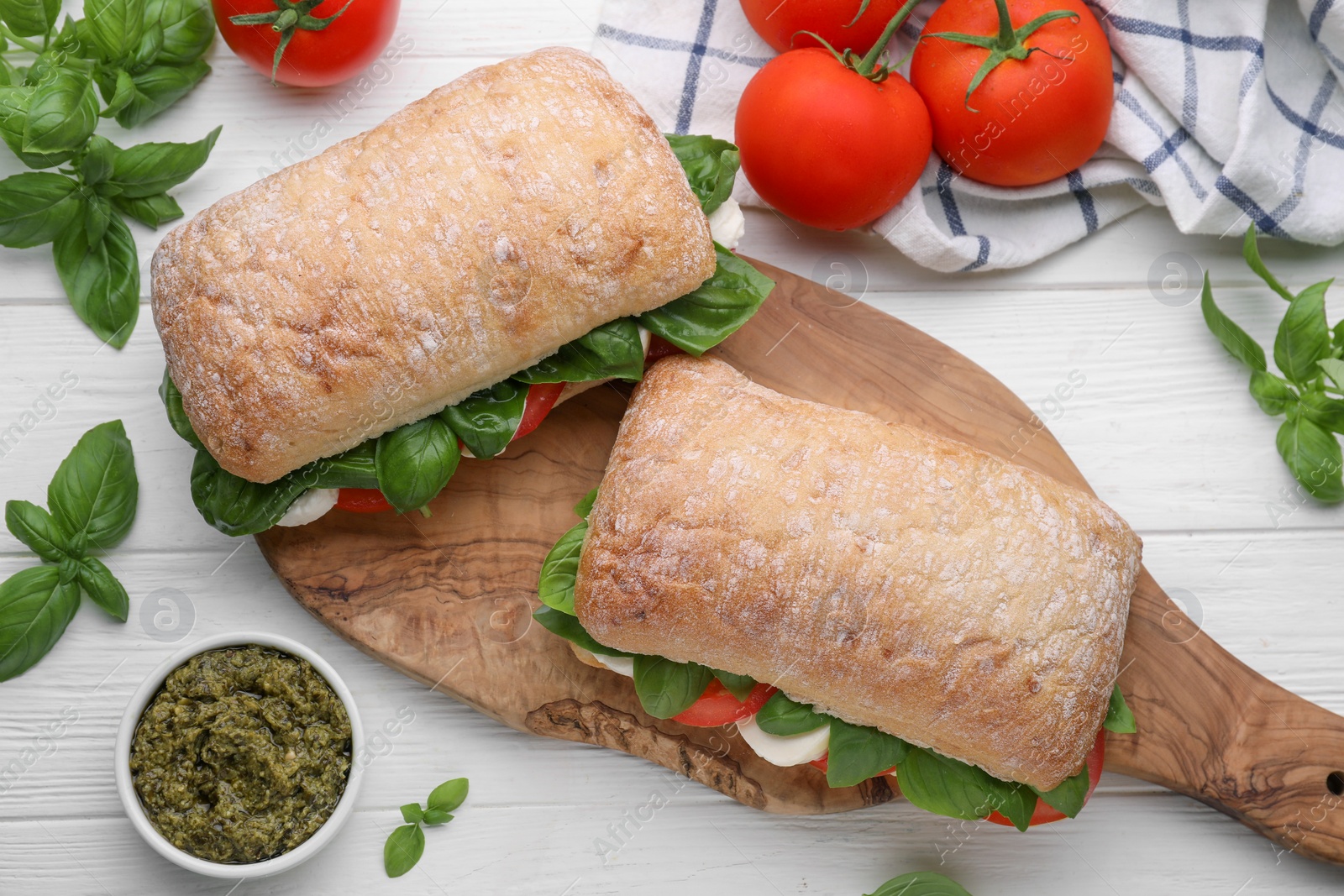 Photo of Delicious Caprese sandwiches with mozzarella, tomatoes, basil and pesto sauce on white wooden table, flat lay