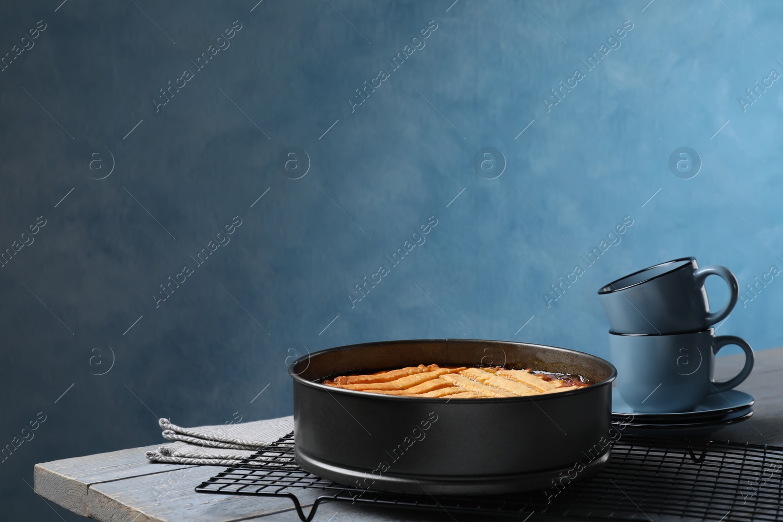 Photo of Delicious apricot pie in baking dish and cups on grey wooden table against blue background. Space for text