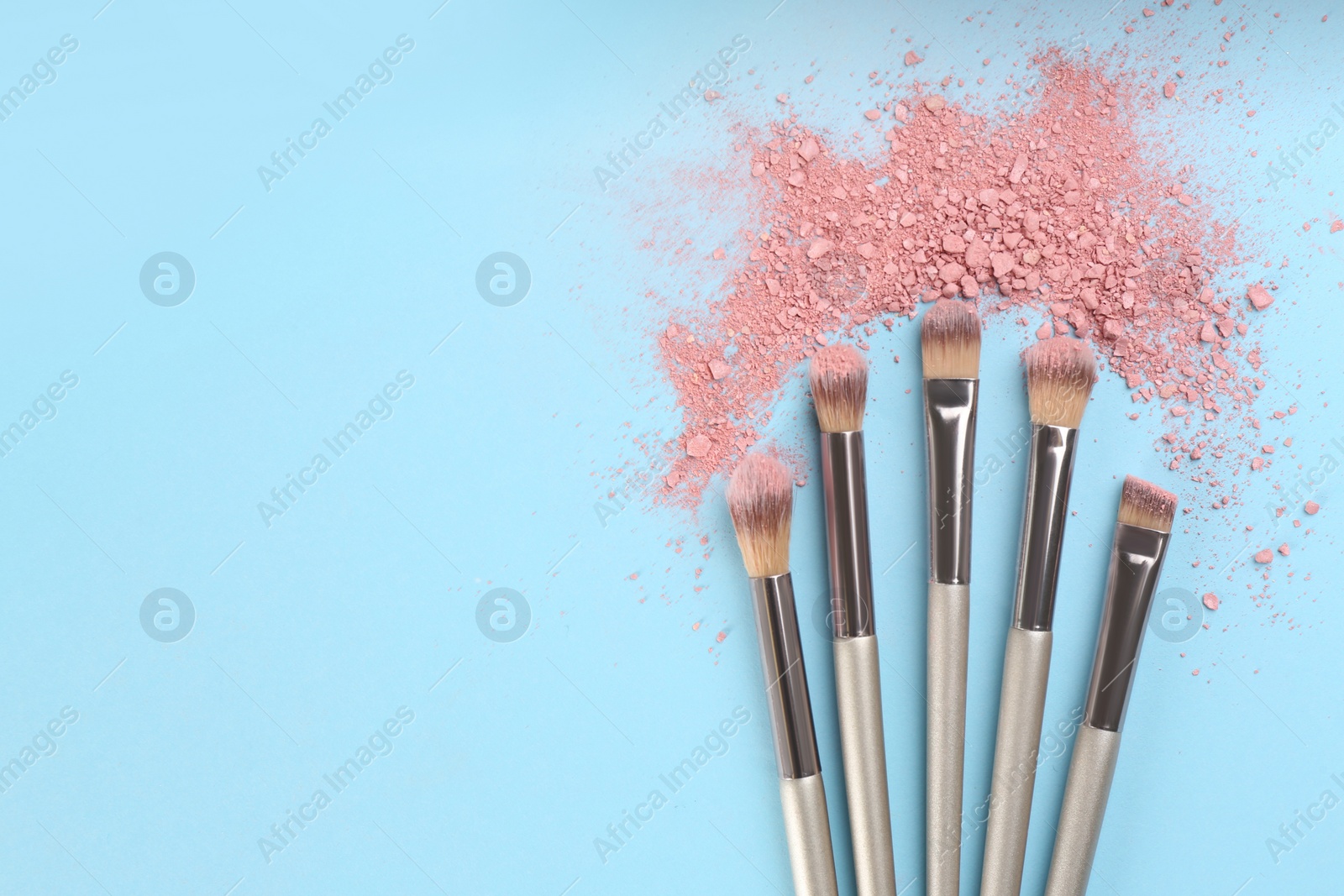 Photo of Makeup brushes and scattered eye shadow on light blue background, flat lay. Space for text