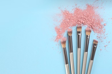 Photo of Makeup brushes and scattered eye shadow on light blue background, flat lay. Space for text