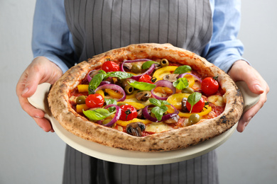 Woman holding tasty vegetable pizza on light grey background, closeup