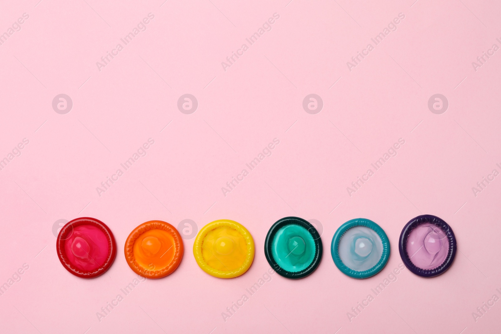 Photo of Flat lay composition with colorful condoms on pink background, space for text. LGBT concept