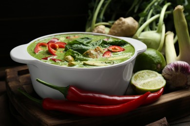 Saucepan with delicious green curry chicken soup and different ingredients on wooden board