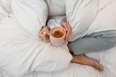 Photo of Woman with cup of coffee and soft blanket on bed, closeup