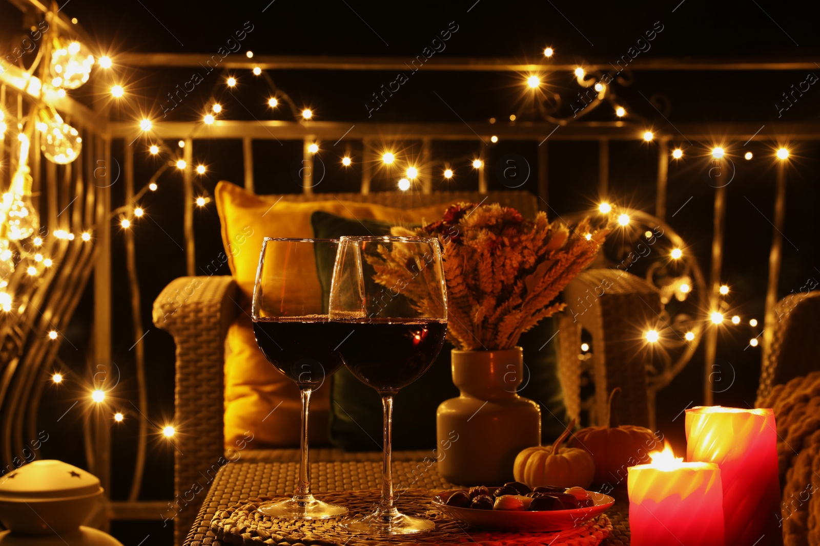 Photo of Glasses of wine, burning candles and decor on rattan table. Autumn evening on terrace