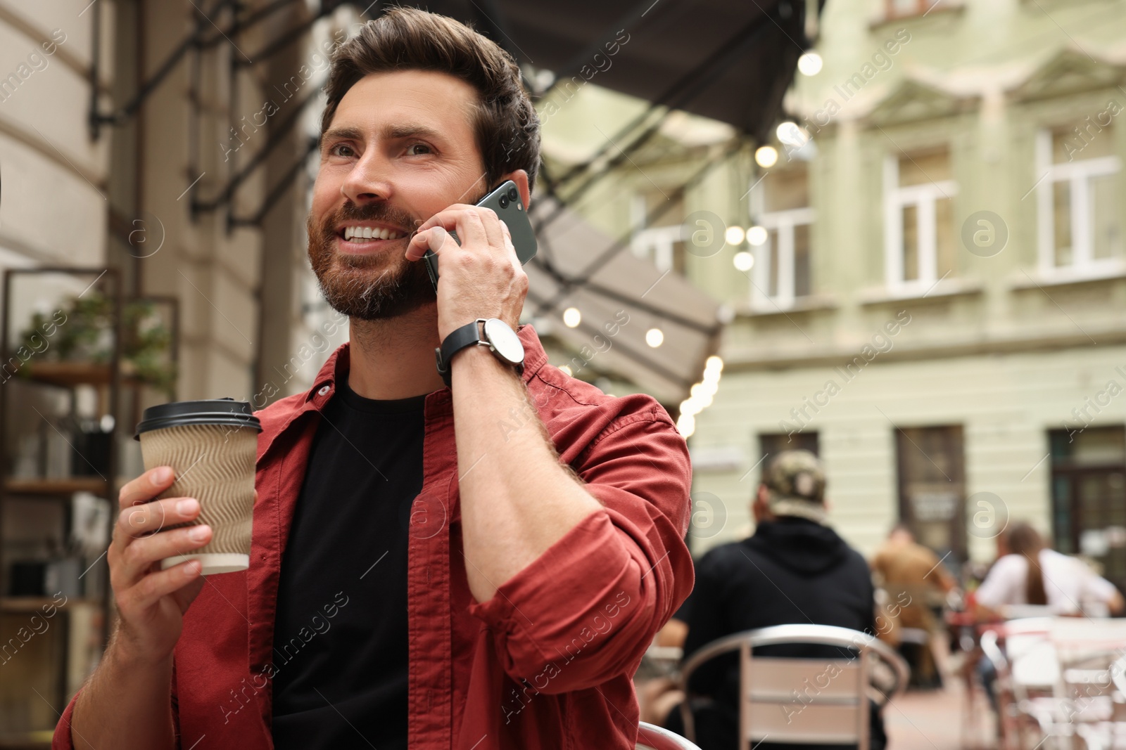 Photo of Handsome man with cup of coffee talking on smartphone outdoors, space for text