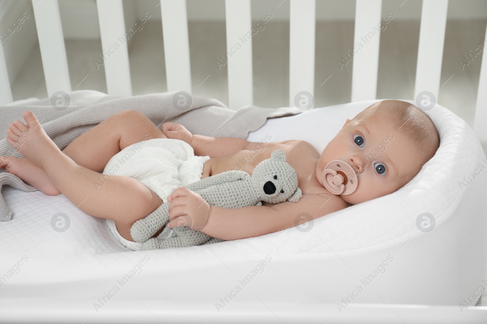 Photo of Cute little baby with pacifier and toy bear lying in crib