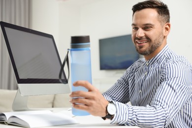 Photo of Man taking transparent plastic bottle of water while working on computer in office