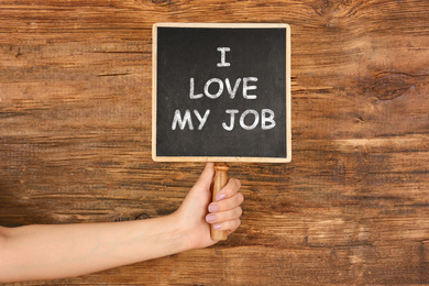 Image of Employee engagement concept. Woman holding chalkboard with text I Love My Job on wooden background, closeup