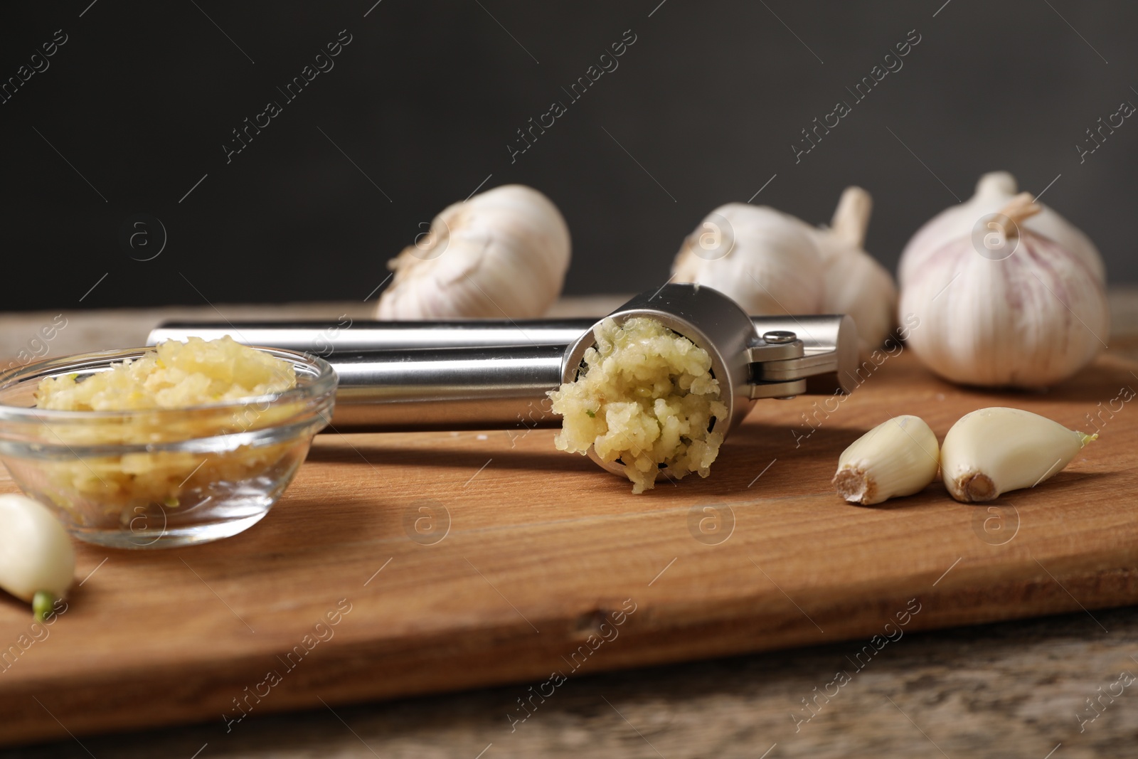 Photo of Garlic press, cloves and mince on wooden table, closeup