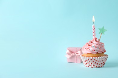 Birthday cupcake with burning candle, gift box and topper on light blue background. Space for text