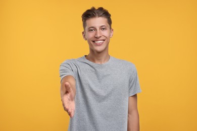 Photo of Happy man welcoming and offering handshake on orange background