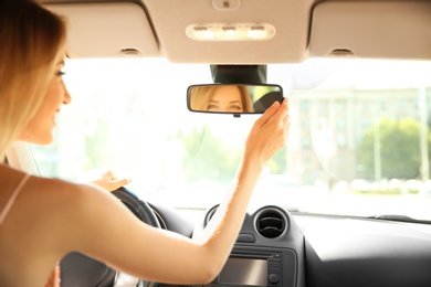 Young woman adjusting rearview mirror in car