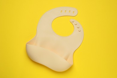 Photo of Beige silicone baby bib on yellow background, top view. First food
