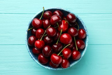 Fresh ripe cherries in bowl on turquoise wooden table, top view