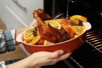 Photo of Woman taking baked chicken with orange slices out of oven, closeup