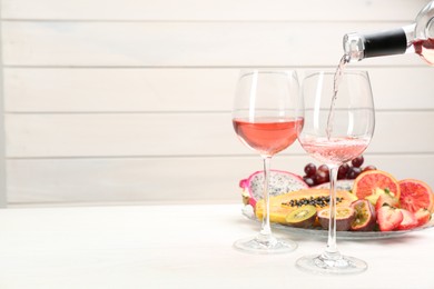 Photo of Pouring wine into glasses and delicious exotic fruits on white wooden table. Space for text