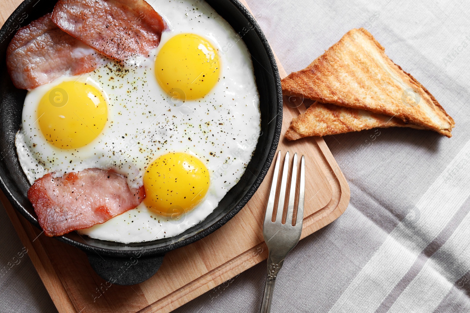 Photo of Tasty fried eggs with bacon and toasts on fabric, flat lay