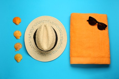 Beach towel, hat and sunglasses on light blue background, flat lay