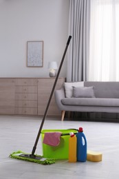 Photo of Bucket, cleaning products and mop on floor in living room
