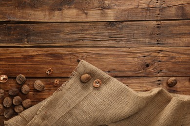 Burlap fabric and walnuts on wooden table, top view. Space for text