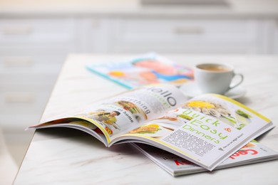 Culinary magazines and cup of coffee on table in kitchen