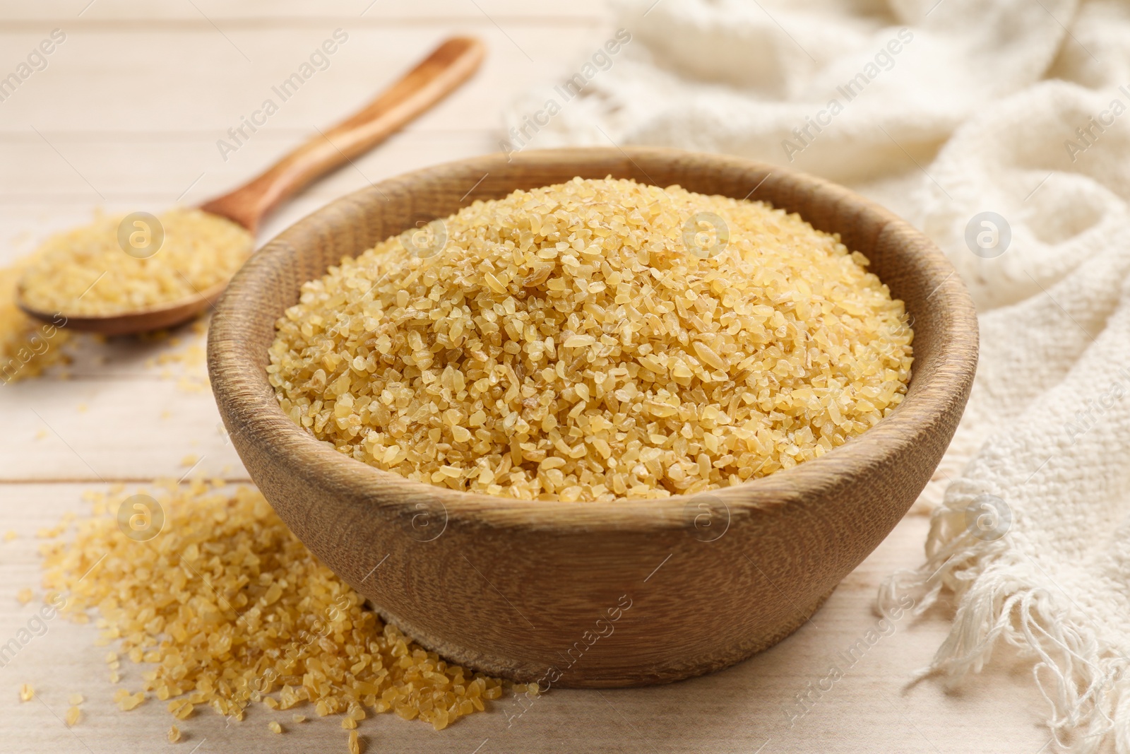 Photo of Bowl and spoon with raw bulgur on light wooden table