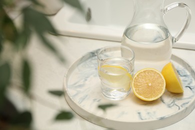 Photo of Jug, glass with clear water and lemons on white table in kitchen
