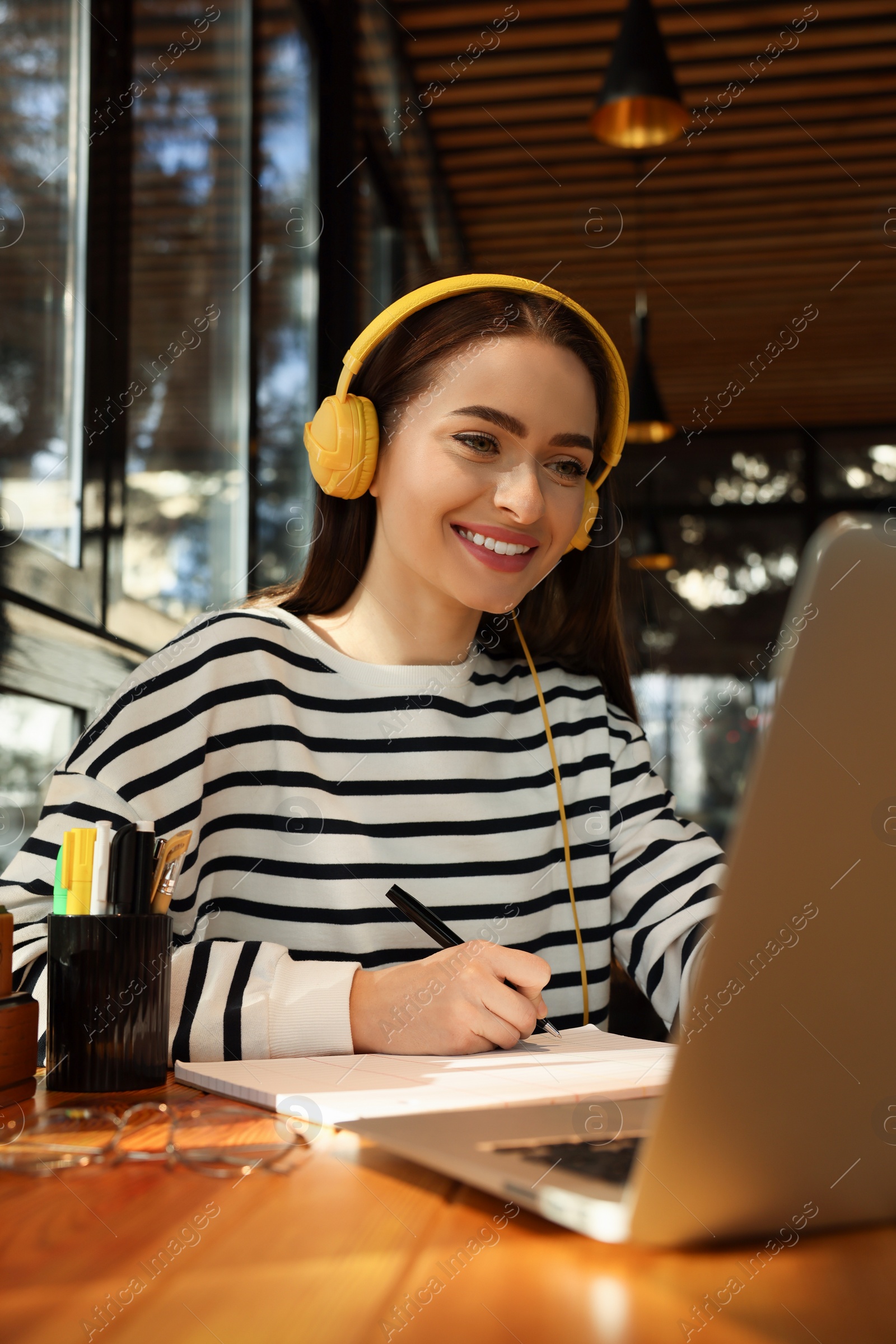 Photo of Young female student with laptop and headphones studying at table in cafe