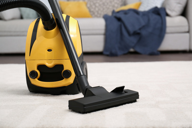 Photo of Modern yellow vacuum cleaner on carpet indoors, space for text