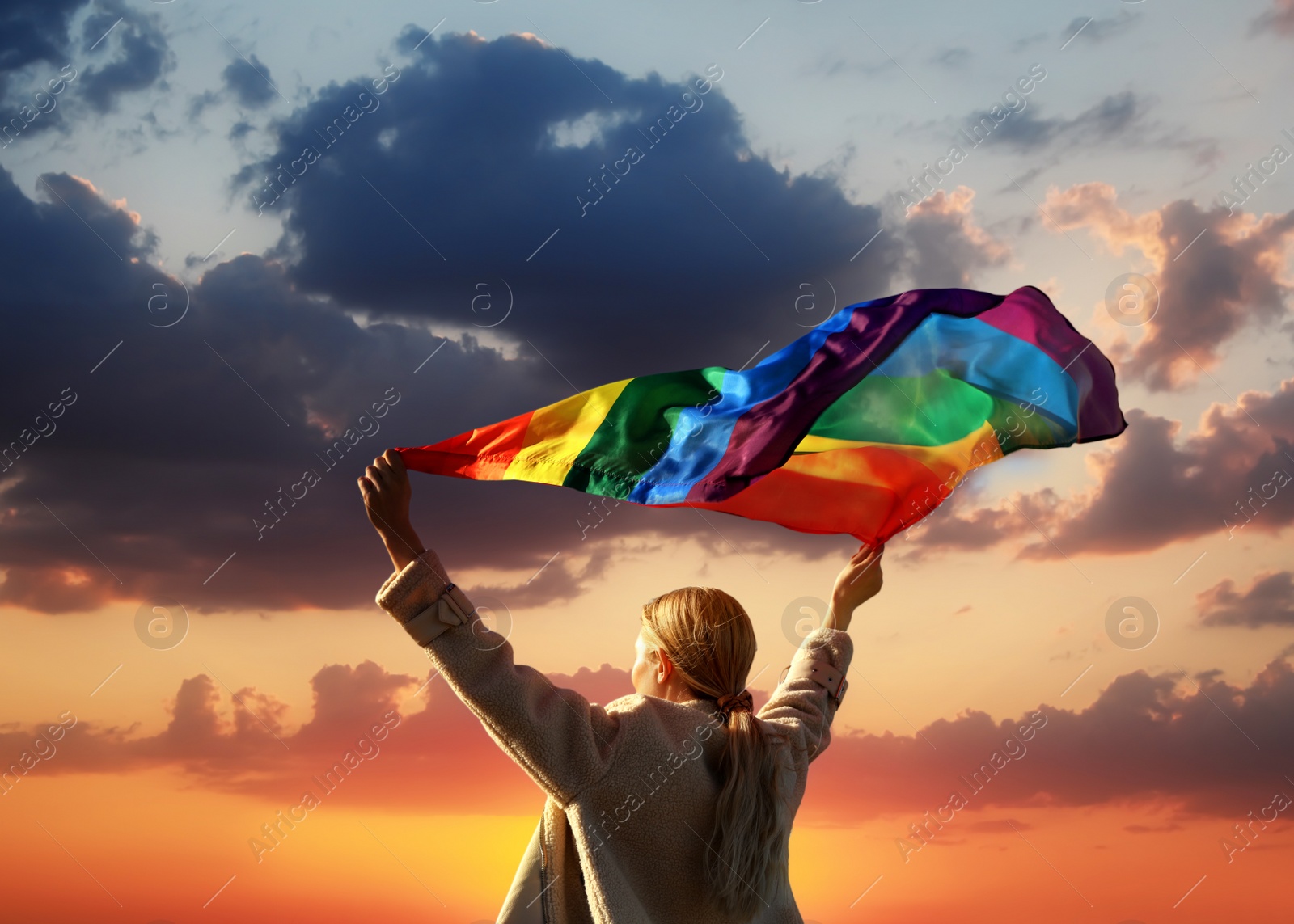 Image of Woman with bright LGBT flag against sky at sunset