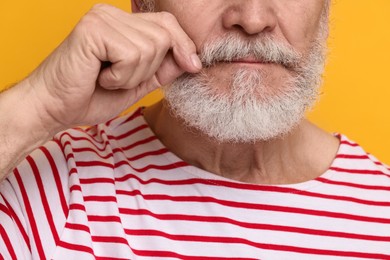 Photo of Man touching mustache on orange background, closeup