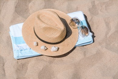 Photo of Straw hat with seashells, sunglasses and beach towel on sand
