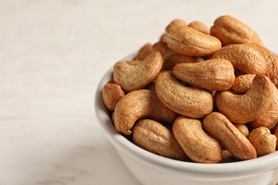 Photo of Tasty cashew nuts in bowl on table, closeup. Space for text