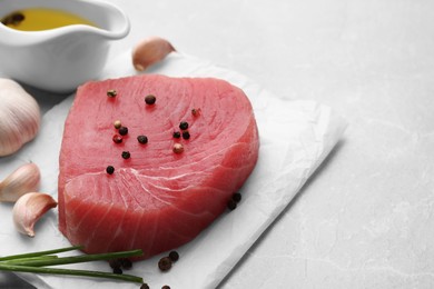 Photo of Raw tuna fillet and spices on light gray table. Space for text