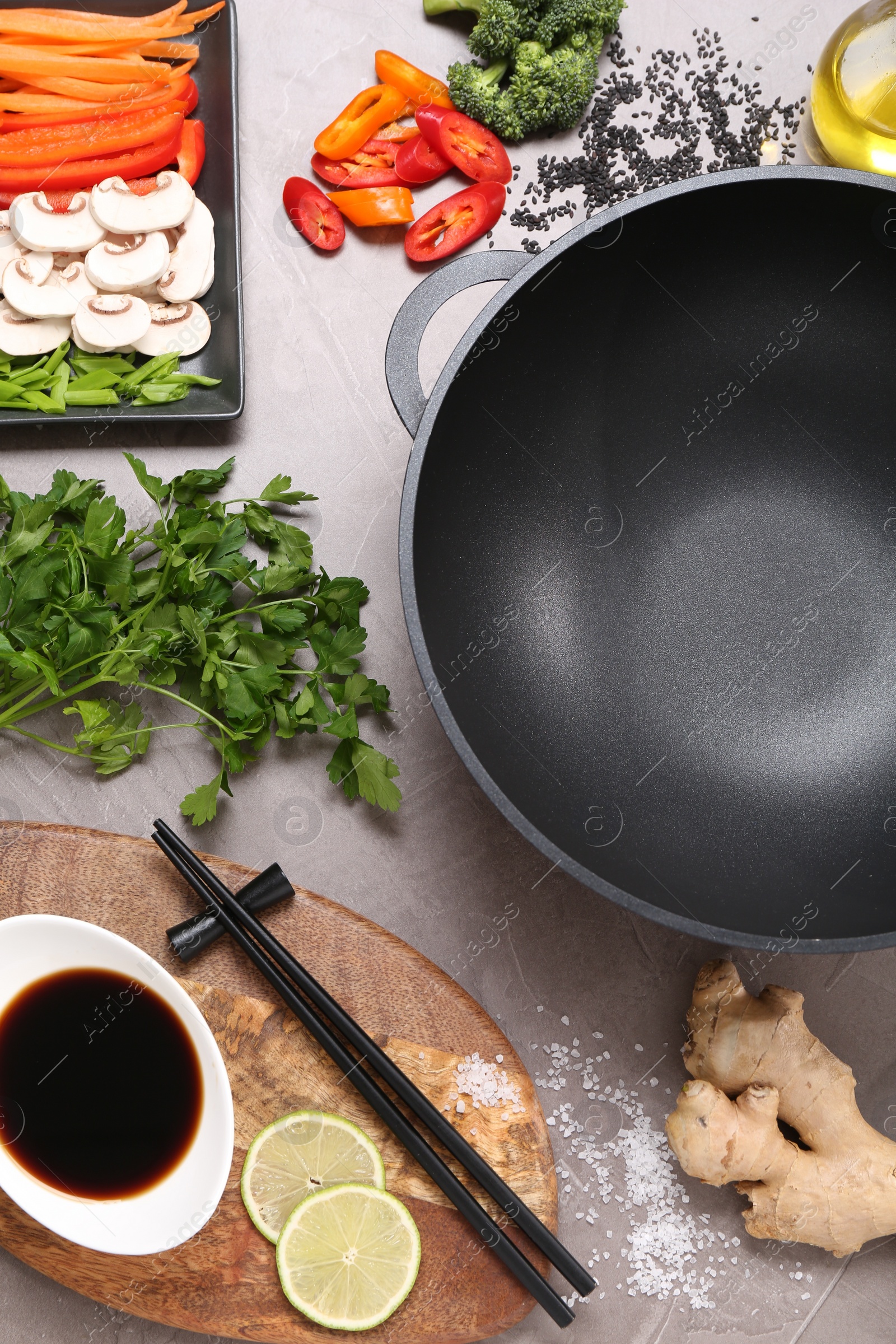 Photo of Wok, chopsticks and different products on grey textured table, flat lay