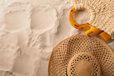 Photo of Straw hat and bag with sunscreen on sand, flat lay. Space for text
